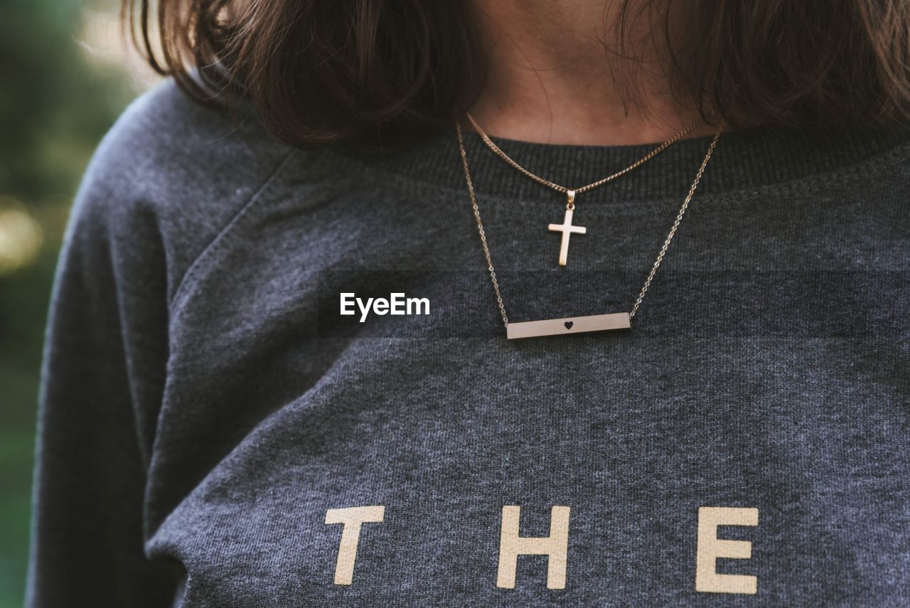 Midsection of teenage girl wearing crucifix necklace with text on t-shirt