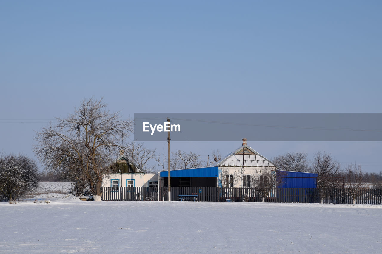 snow, winter, cold temperature, architecture, built structure, building exterior, sky, nature, building, tree, clear sky, no people, blue, day, copy space, plant, white, house, landscape, frozen, environment, scenics - nature, outdoors, bare tree, rural scene, land, travel destinations, sunny