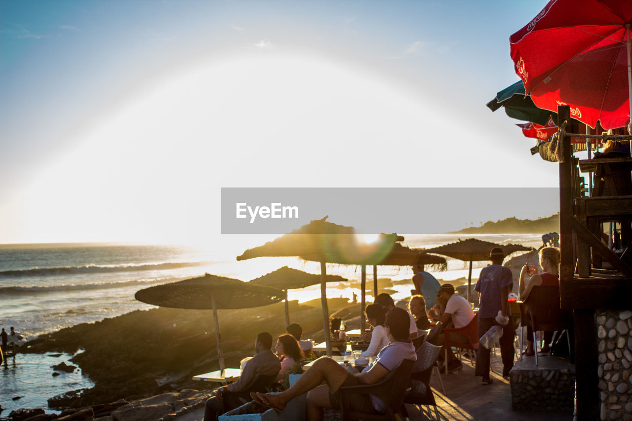 PEOPLE RELAXING ON BEACH AGAINST SKY