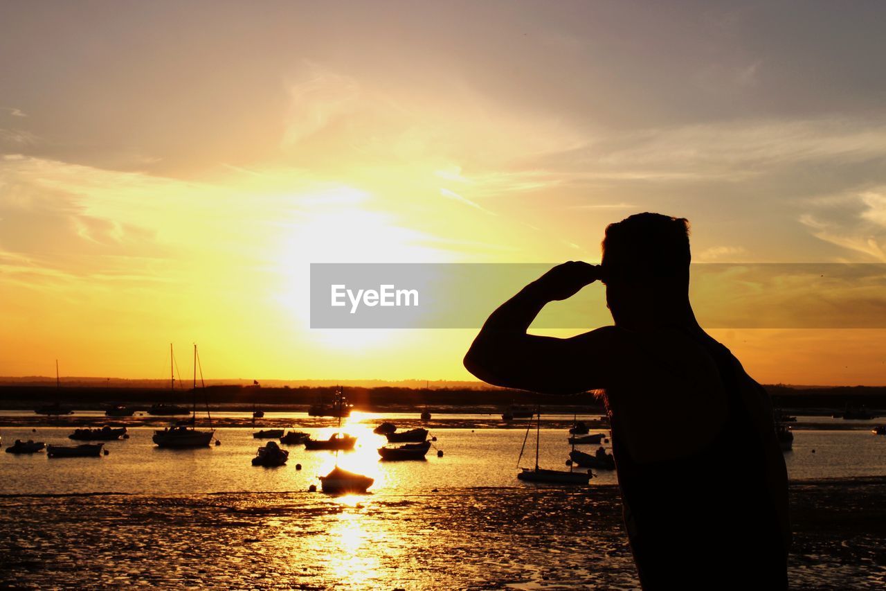 SILHOUETTE MAN STANDING ON BEACH AGAINST ORANGE SKY