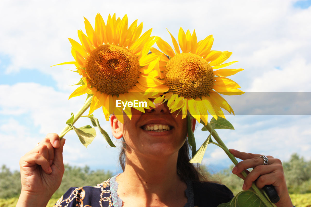 Happy nice woman hides behind yellow blooming sunflowers in summer