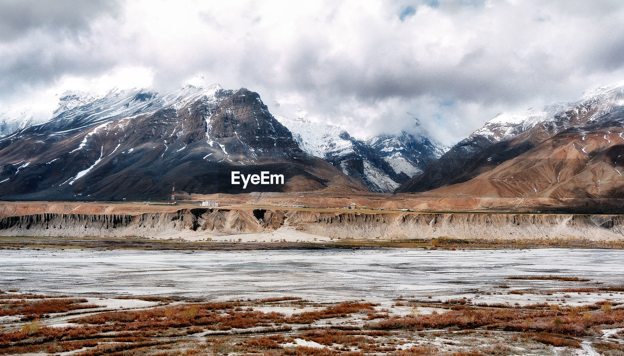 Frozen lake and snowcapped mountains against cloudy sky