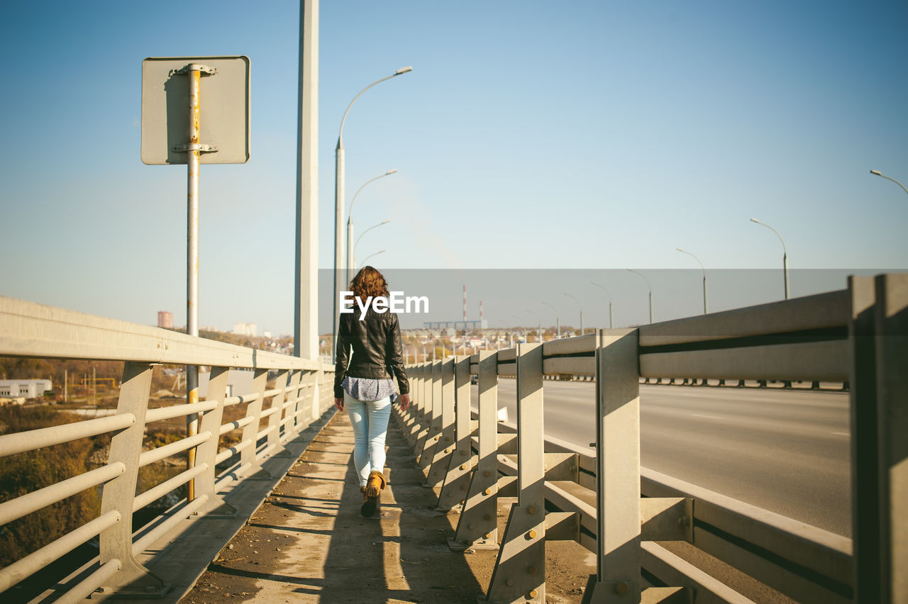 Rear view of young woman walking on bridge against sky