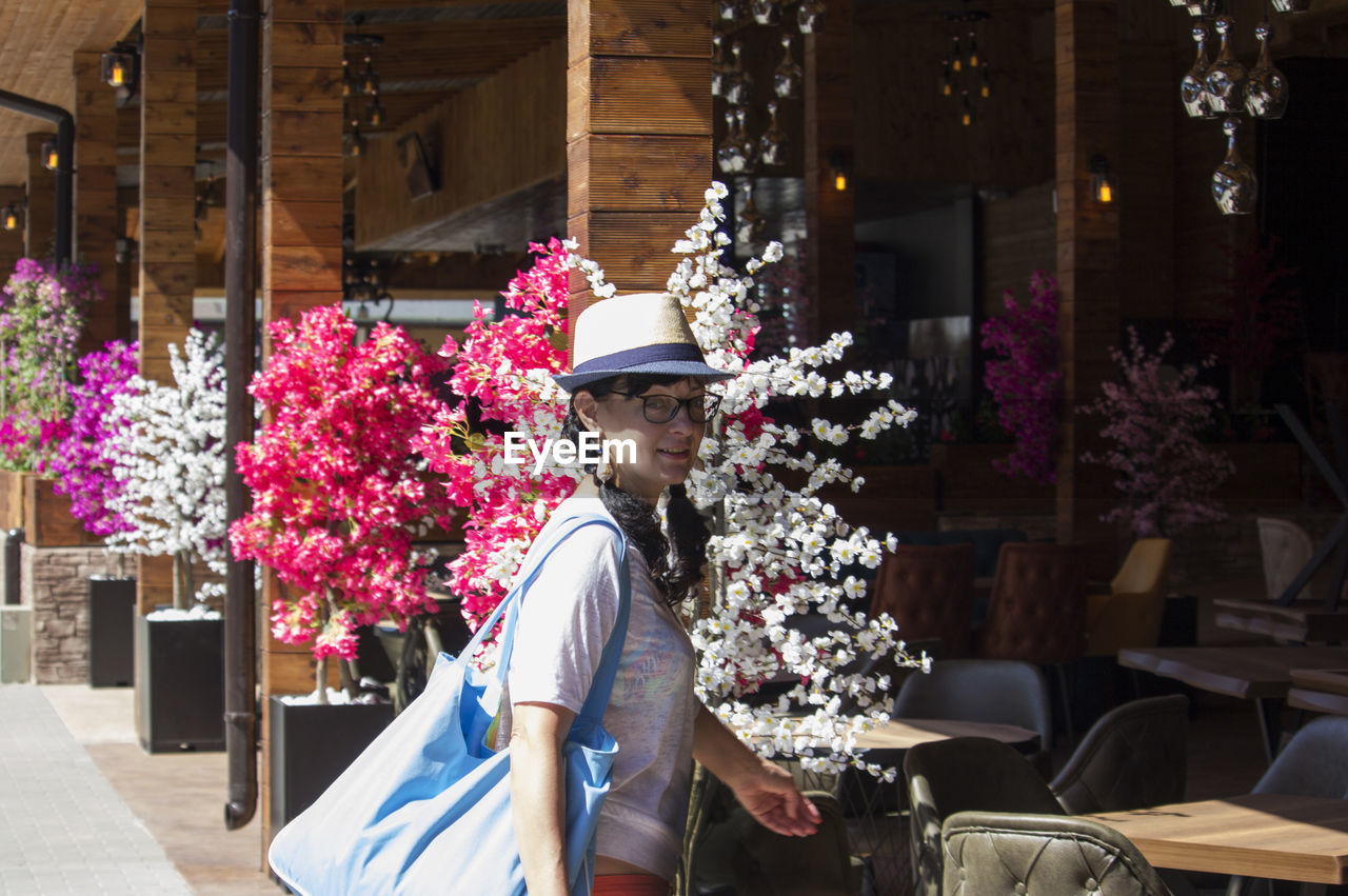 PORTRAIT OF WOMAN STANDING BY POTTED PLANT