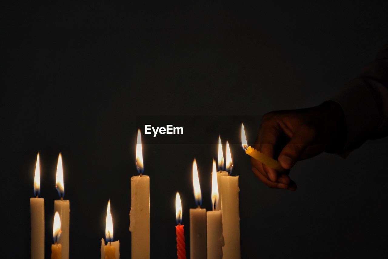 Cropped hand igniting candles in darkroom