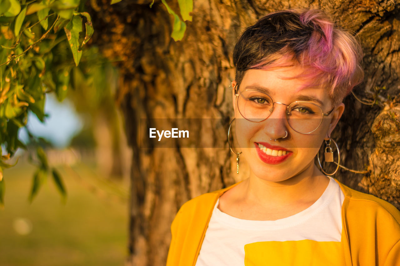 Portrait of smiling young woman against tree trunk