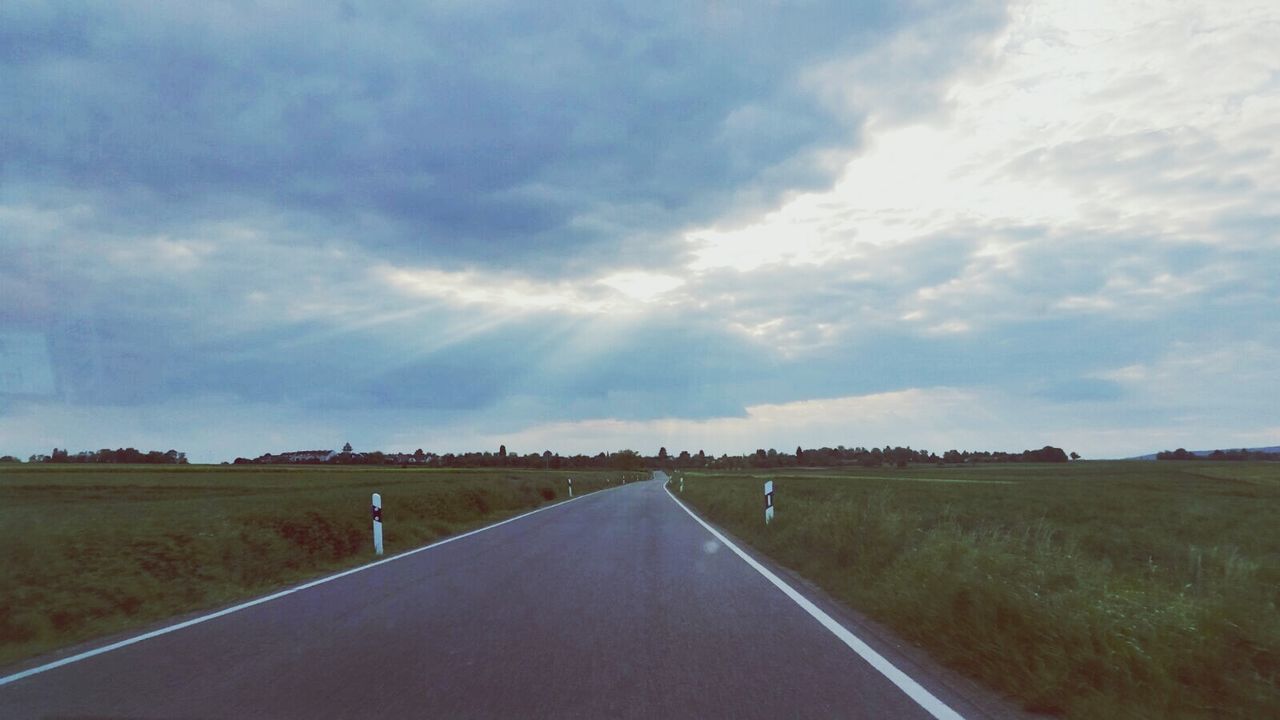 Road passing through field against cloudy sky