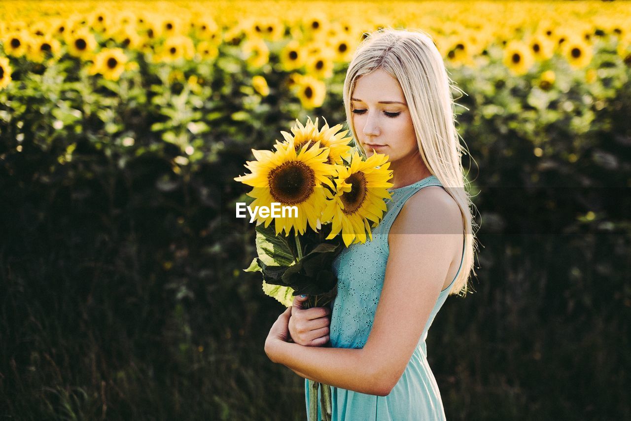 Young woman holding sunflowers on field