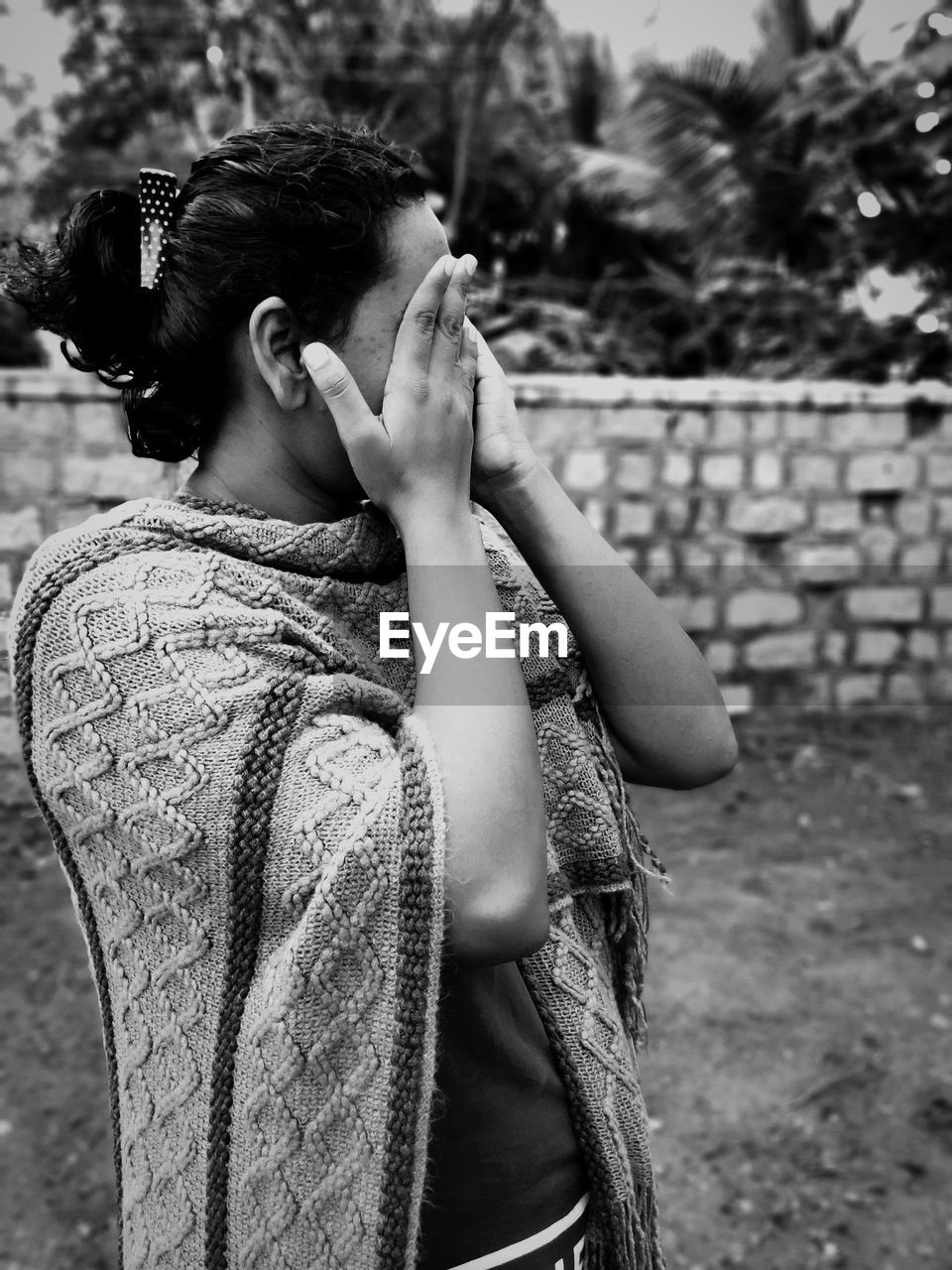 Woman with hands covering eyes standing on land against trees