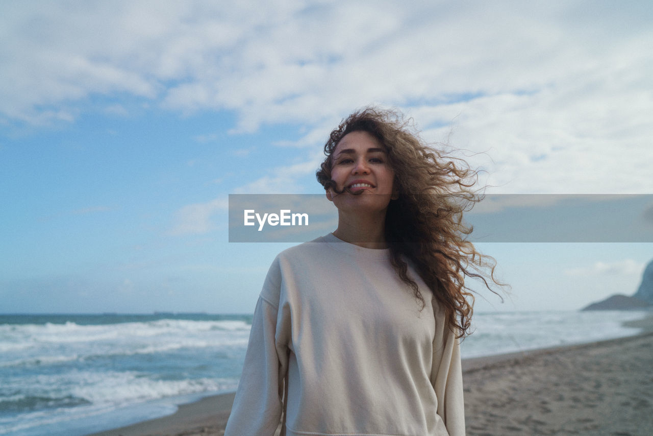 Happy young woman standing on beach against sky