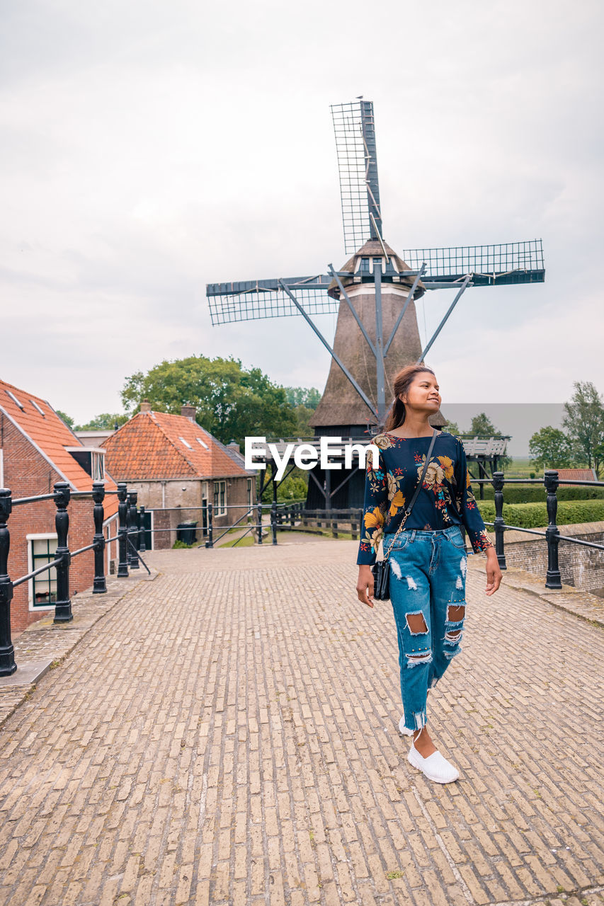 Mid adult woman walking on footpath against traditional windmill