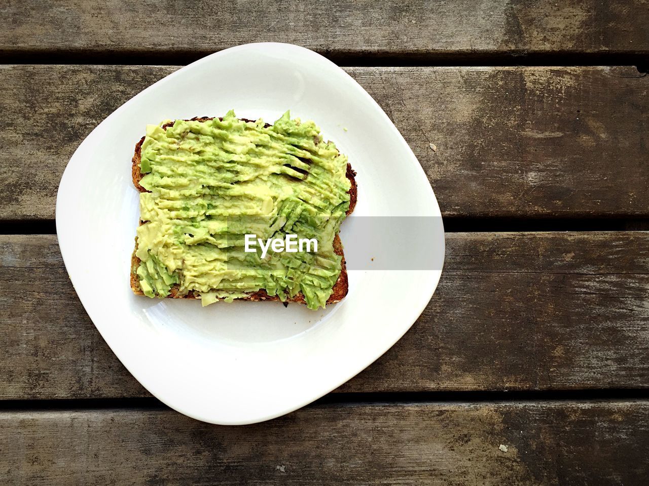 High angle view of avocado and bread in plate on wooden table