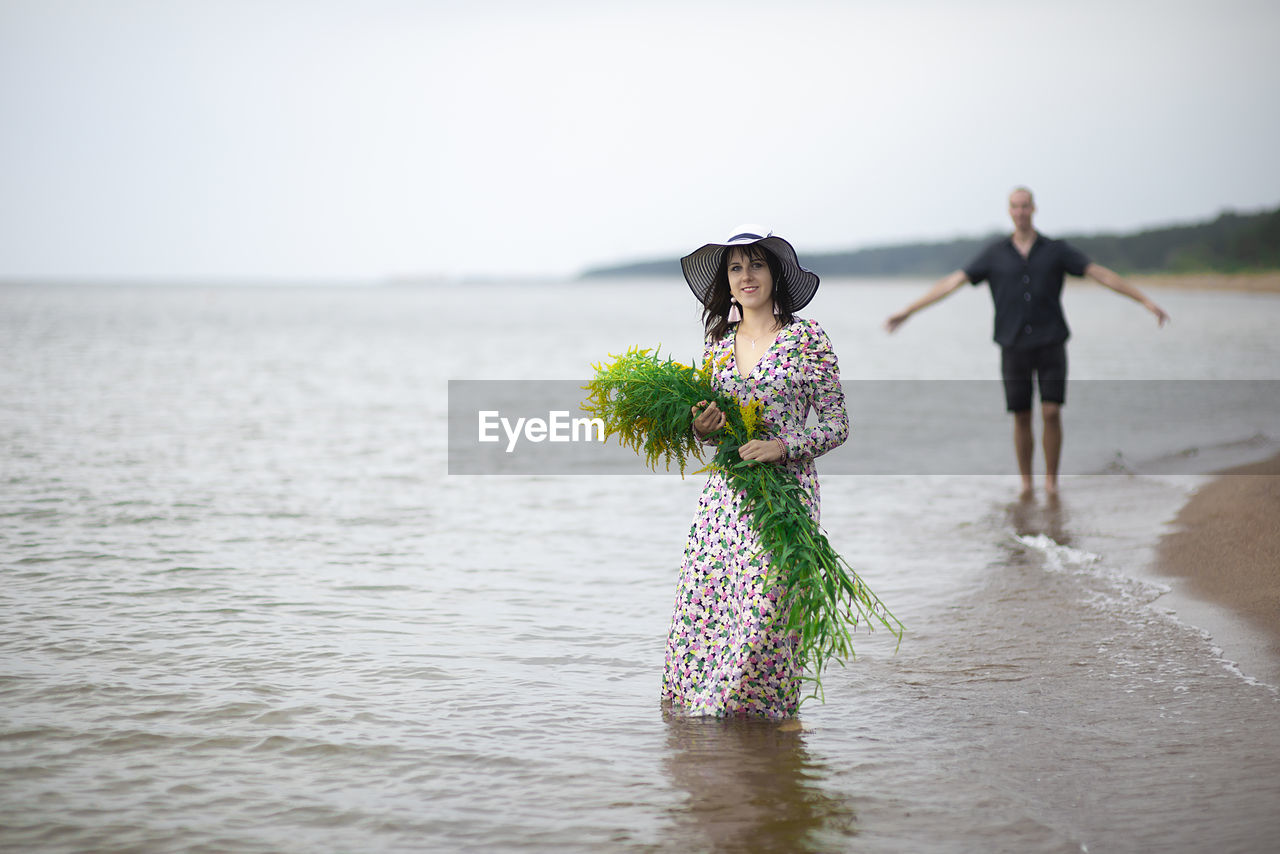 A young  woman holds a large bouquet of wild flowers, against the background of a male silhouette