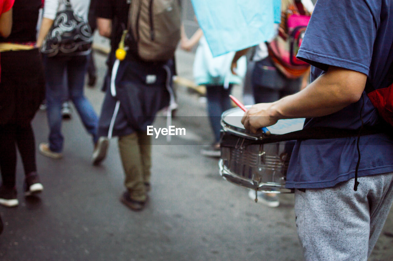 Midsection of man playing drum while walking on street