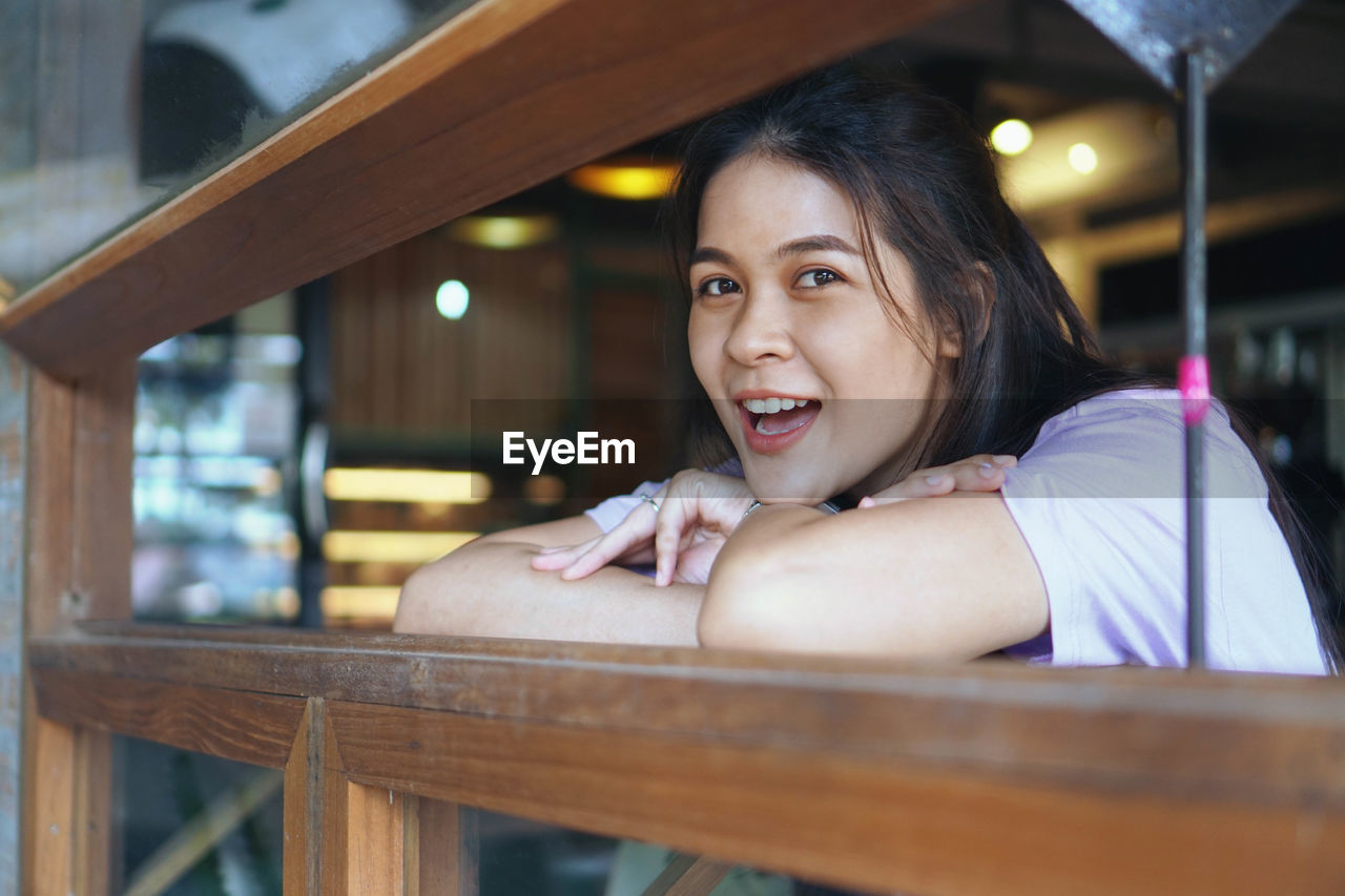 PORTRAIT OF SMILING WOMAN SITTING ON WOOD