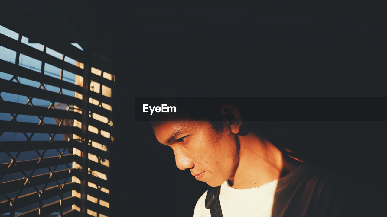 Sunlight falling on young man standing by window in darkroom