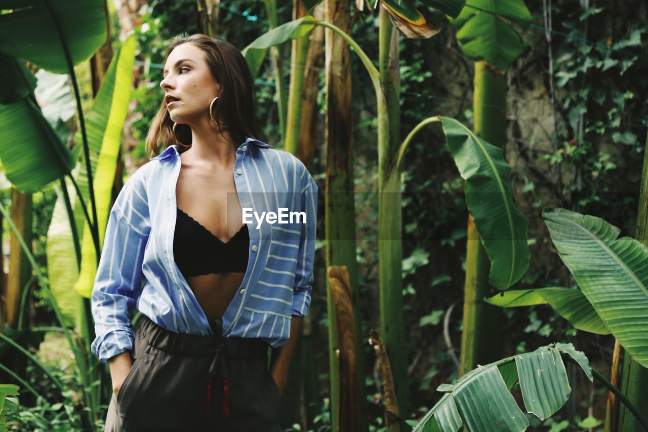 Woman wearing open shirt surrounded by banana leafs