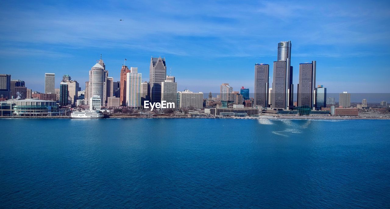 Buildings at waterfront in city against blue sky