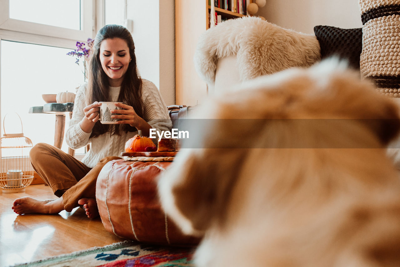 Smiling woman holding mug while sitting on floor at home