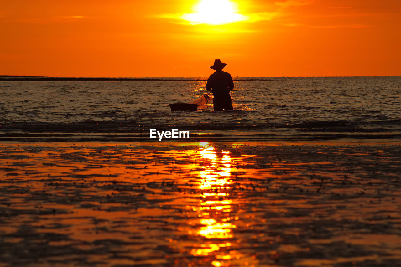 Silhouette man fishing in sea against orange sky