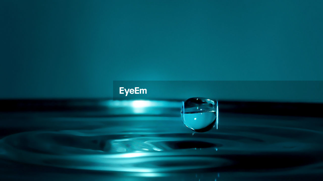 Macro shot of drop falling on water against colored background