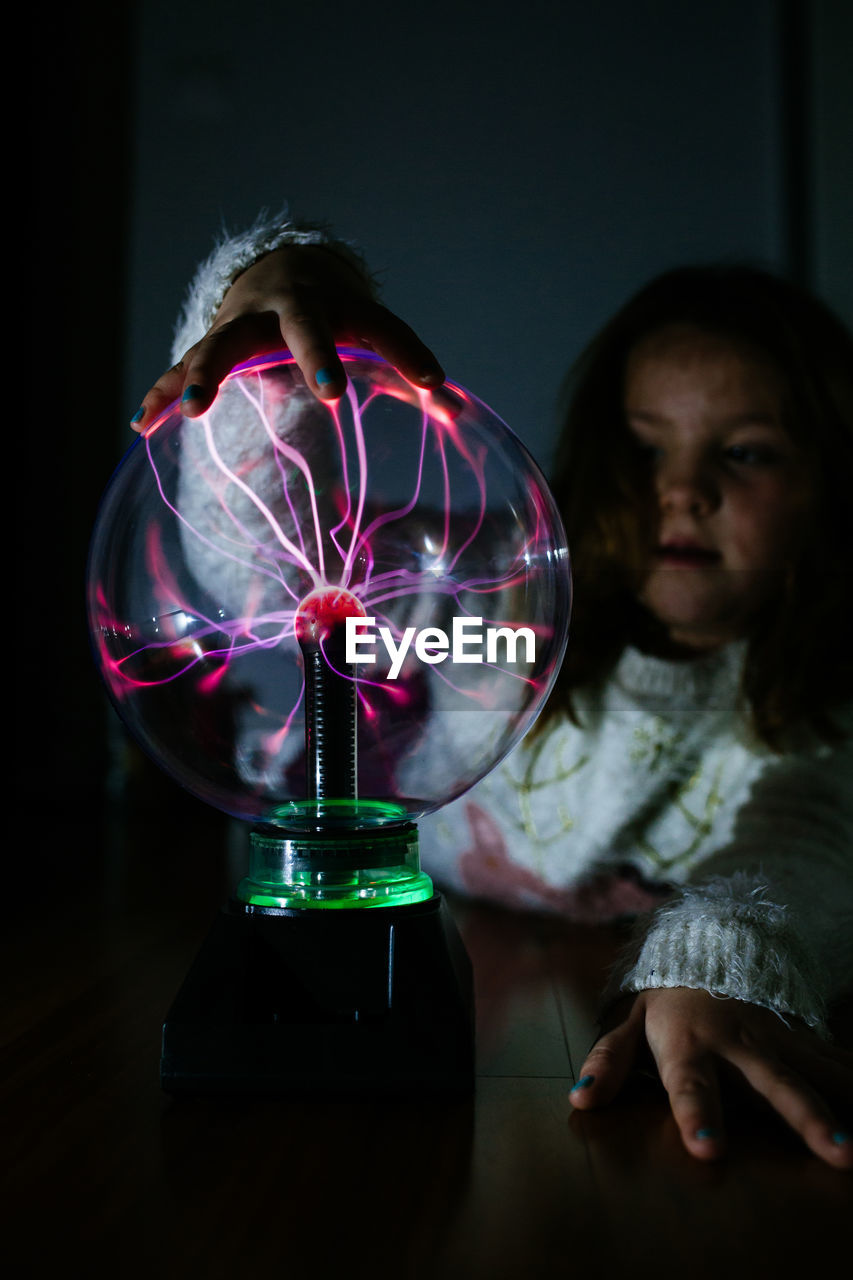 Transparent glass electrical round lamp under hand of adorable girl in dark