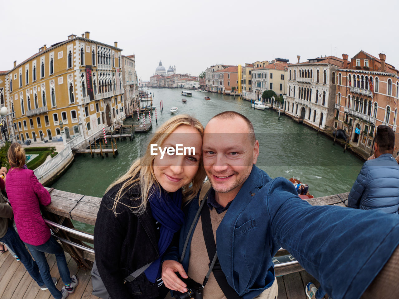 Portrait of smiling couple standing on footbridge over canal