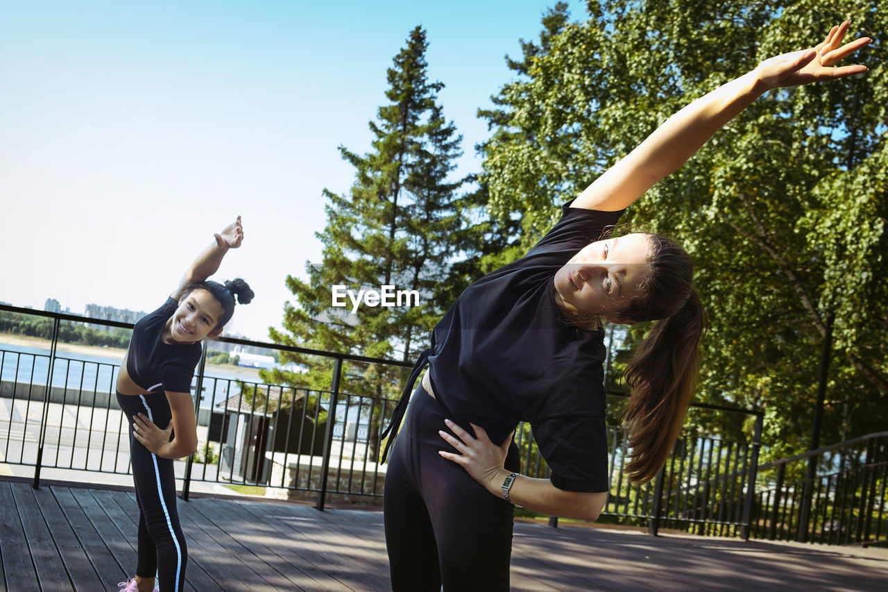 Girl in sportswear on a sunny summer day on the embankment in the park doing fitness and stretching