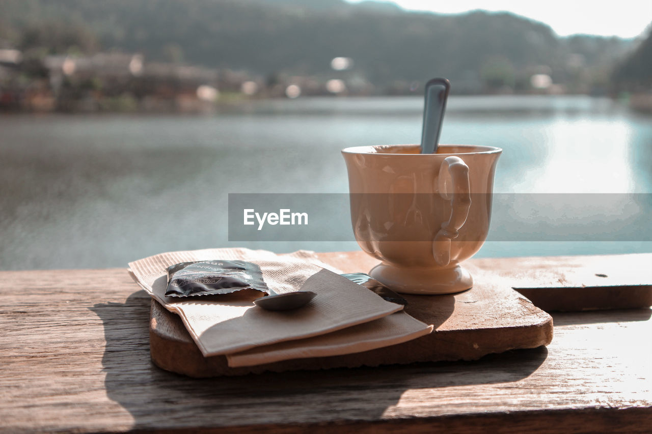 CLOSE-UP OF COFFEE CUP ON TABLE AGAINST WOODEN SURFACE
