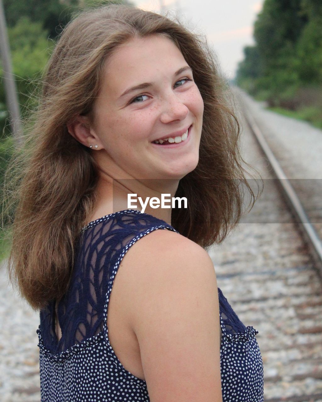 Portrait of smiling young woman standing on railroad track