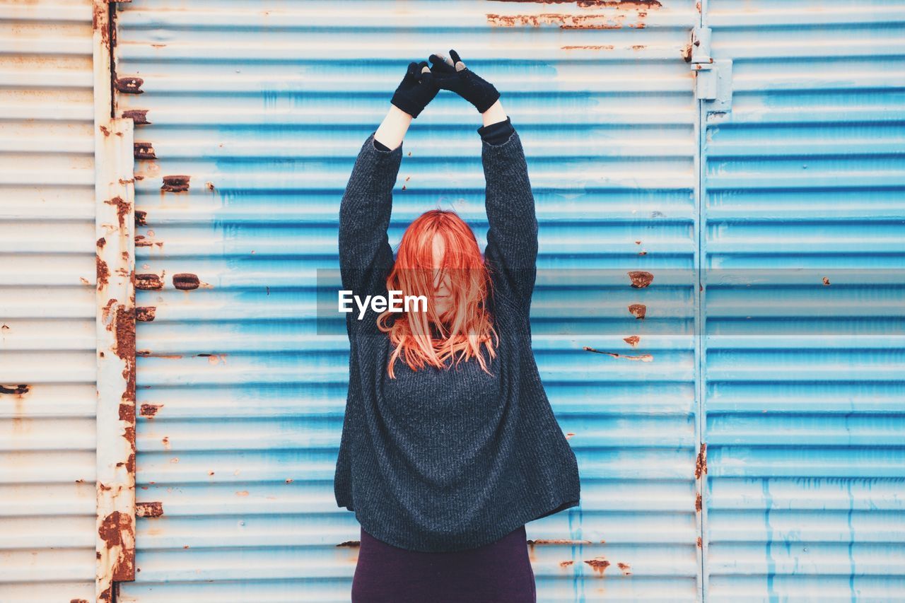 Woman standing with arms raised against blue weathered shutter