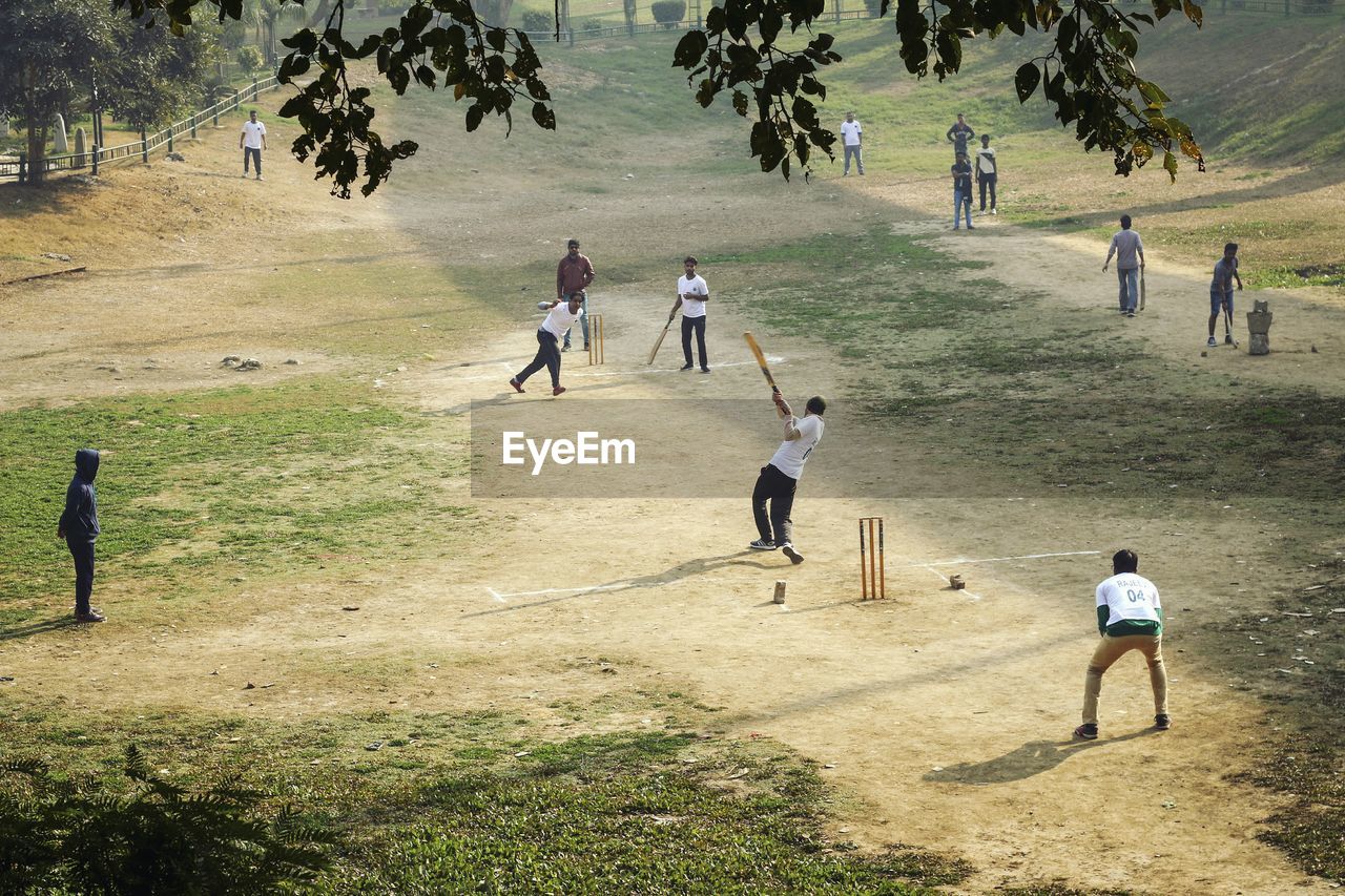 Friends playing cricket on field