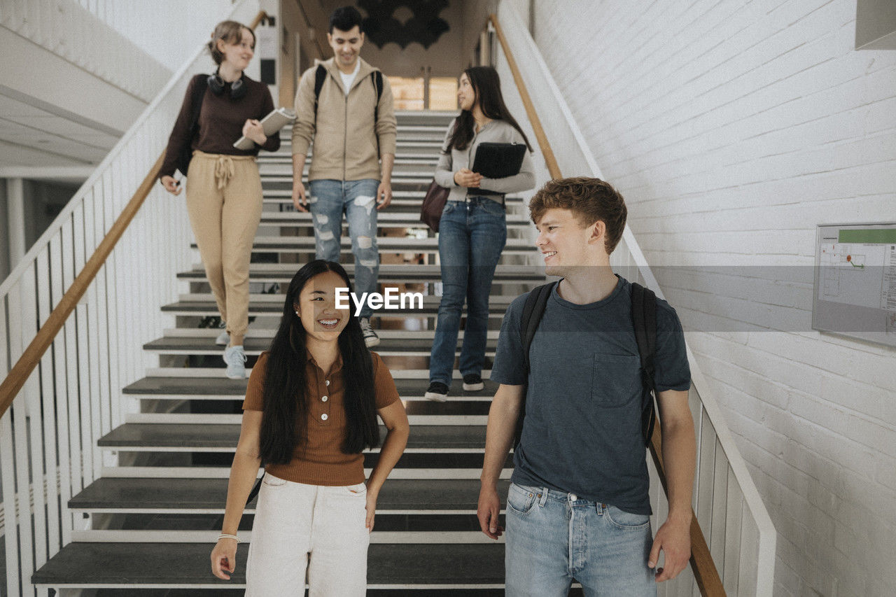 Happy multiracial students talking while moving down on steps in university