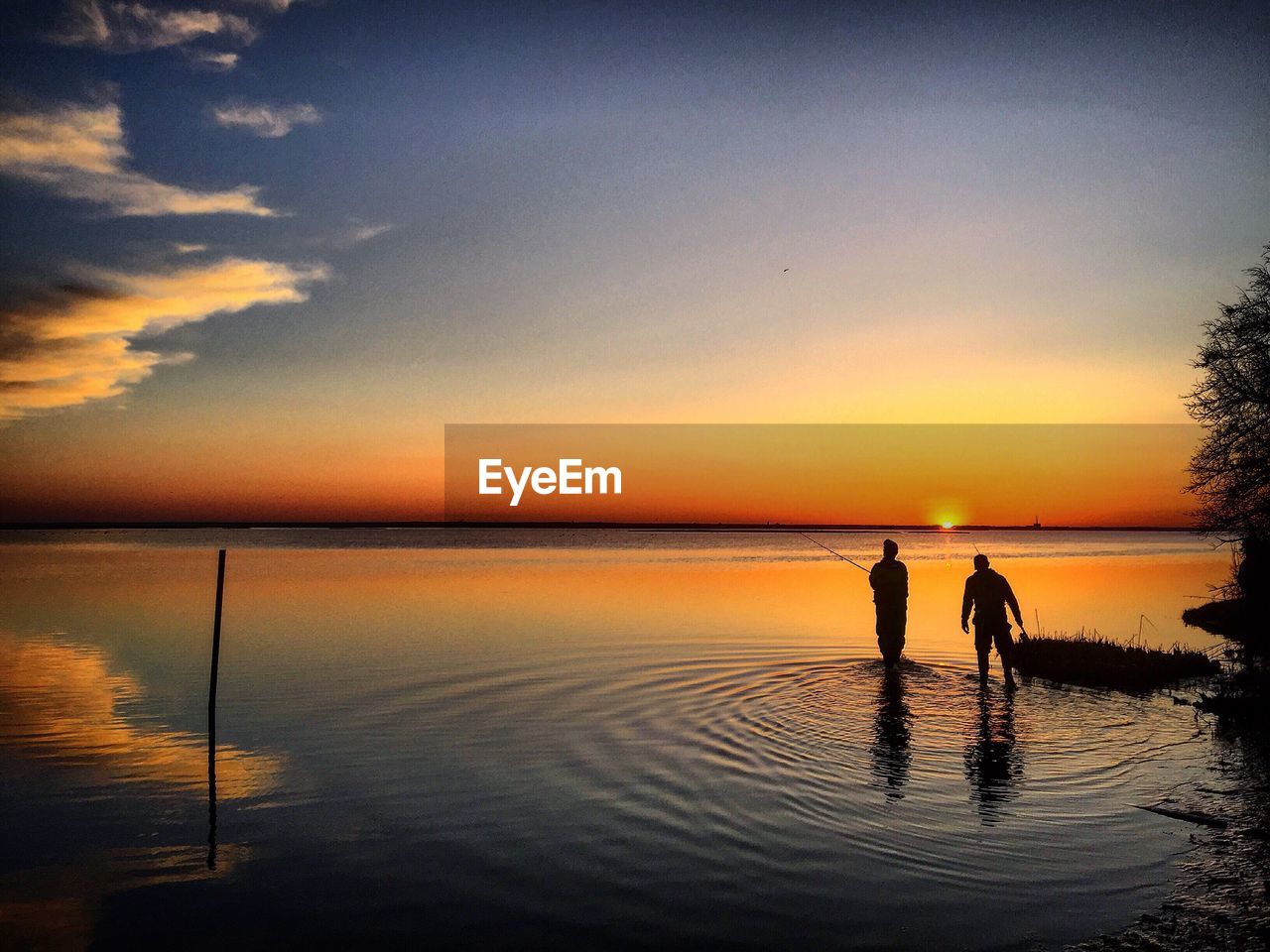 Silhouette people standing in lake against sky during sunset