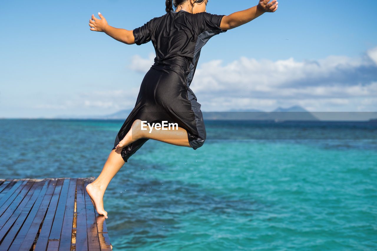 Full length of girl jumping in sea against sky