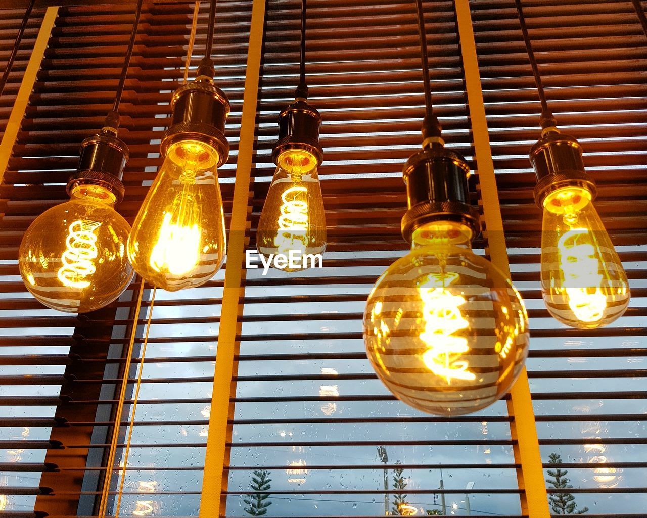 Low angle view of illuminated light bulbs hanging by window