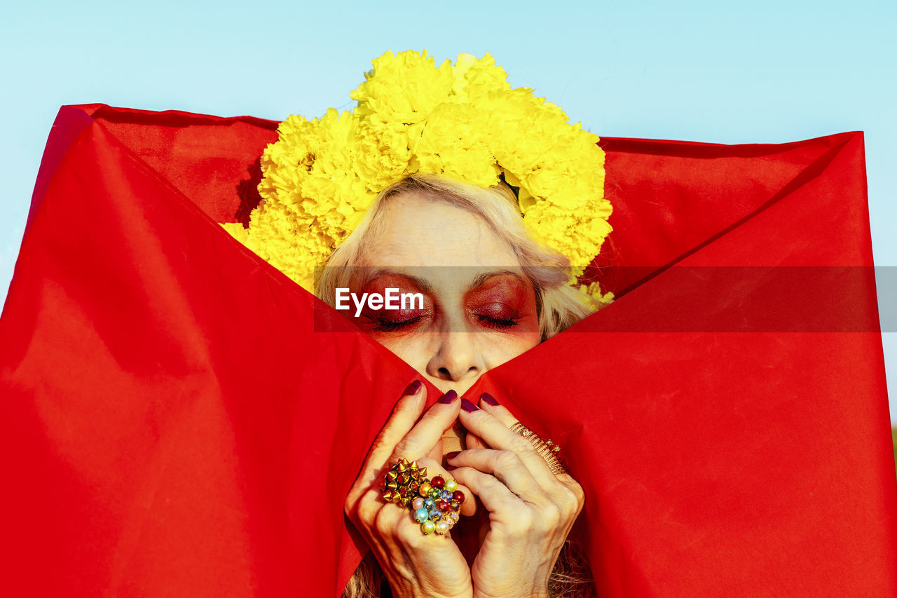 Senior woman with eyes closed wearing marigold flowers on sunny day