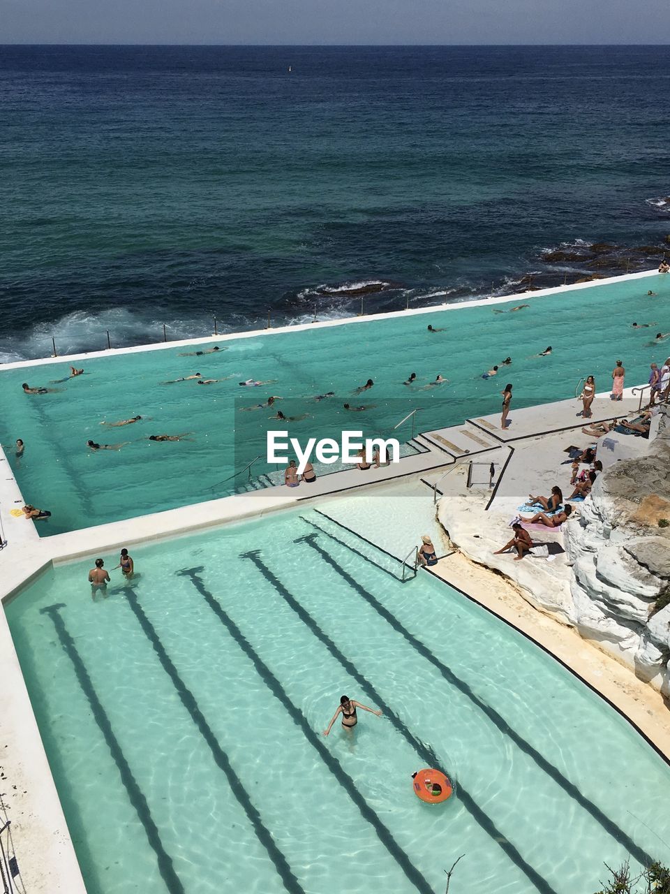 High angle view of people enjoying in infinity pool by sea