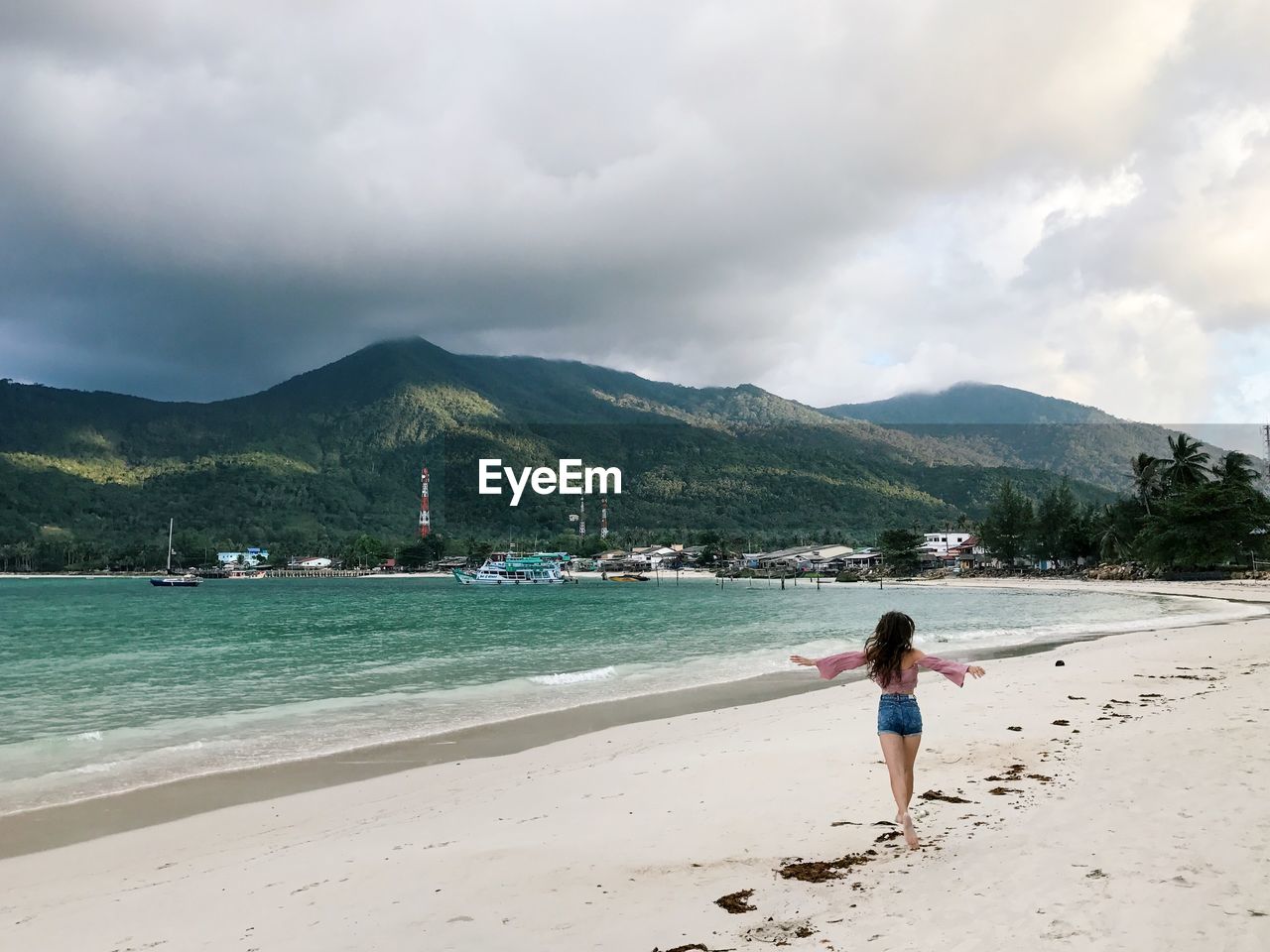 Rear view of woman with arms outstretched at beach against cloudy sky