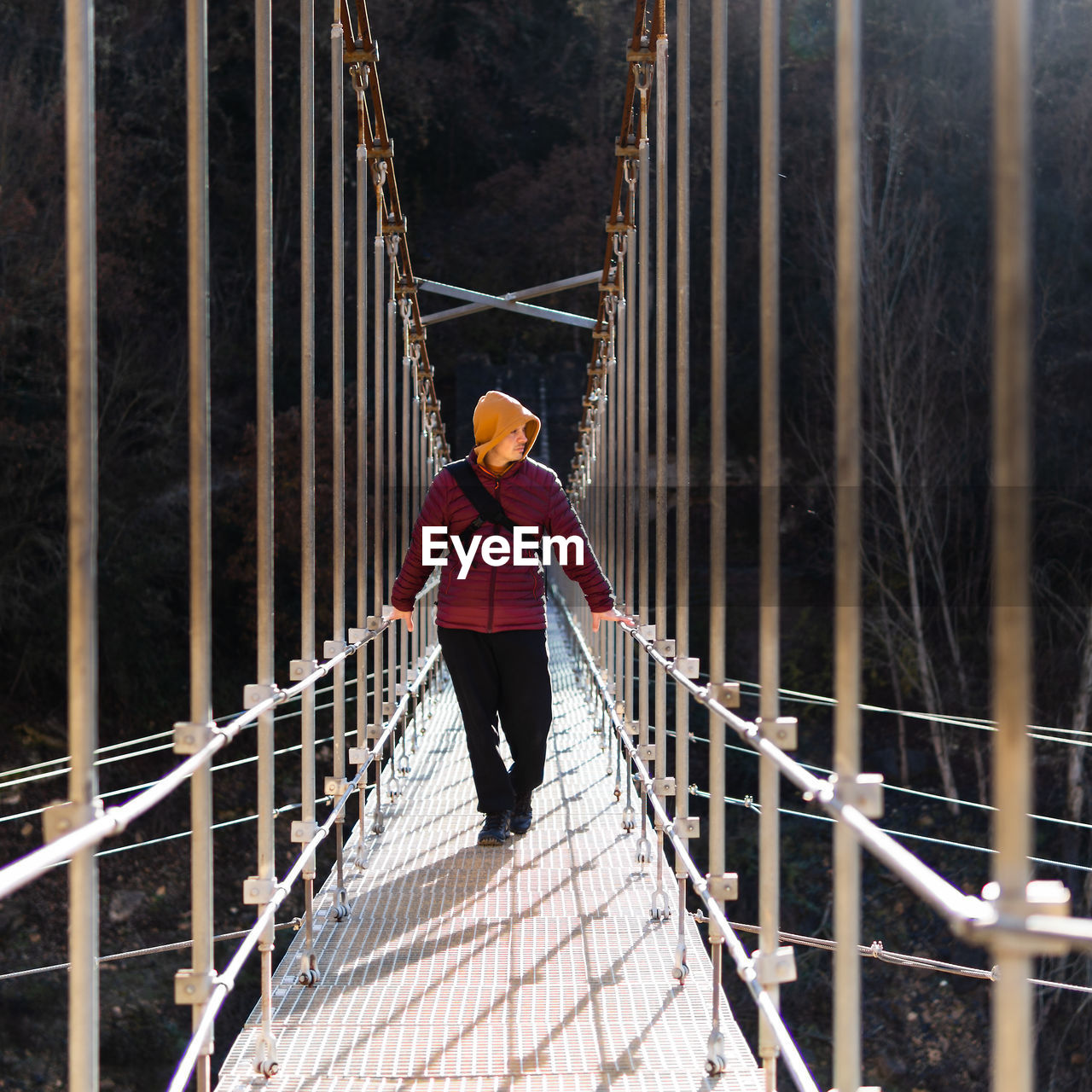 Front view of man wearing warm clothes crossing a suspension bridge