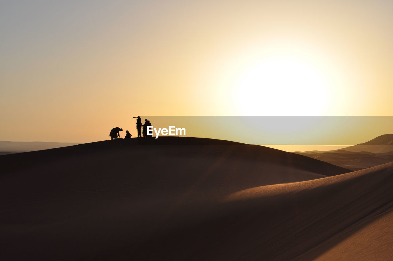 Silhouette people at desert against clear sky during sunset