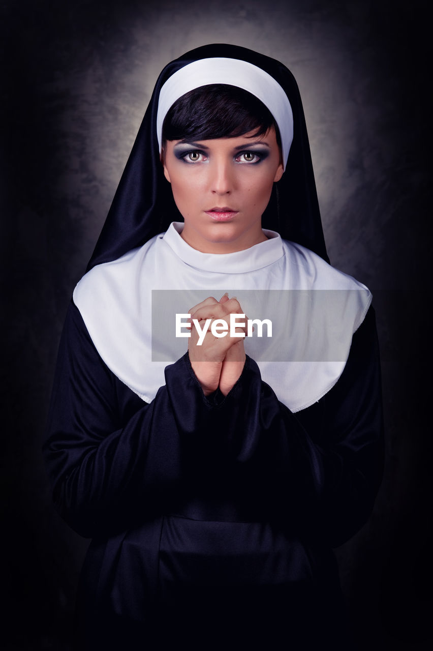 Portrait of nun praying while standing against black background