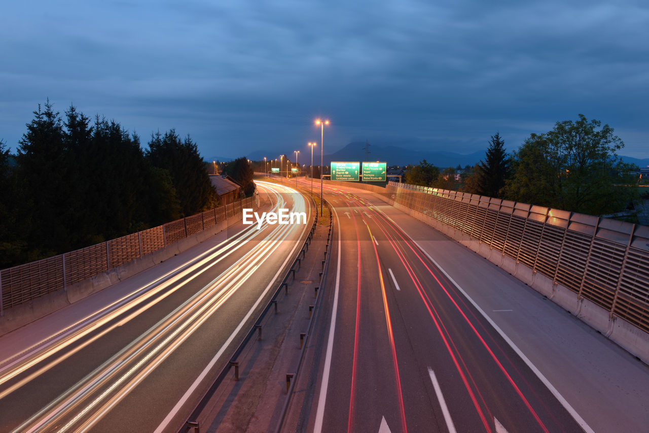 Light trails of vehicles on city street against cloudy sky