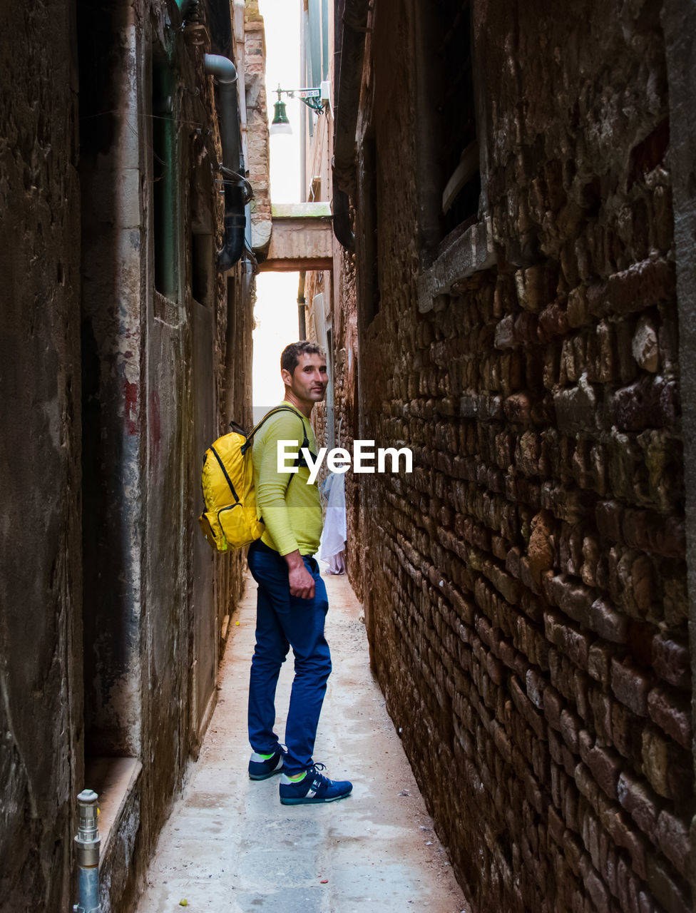 Full length side view of man with backpack standing in alley