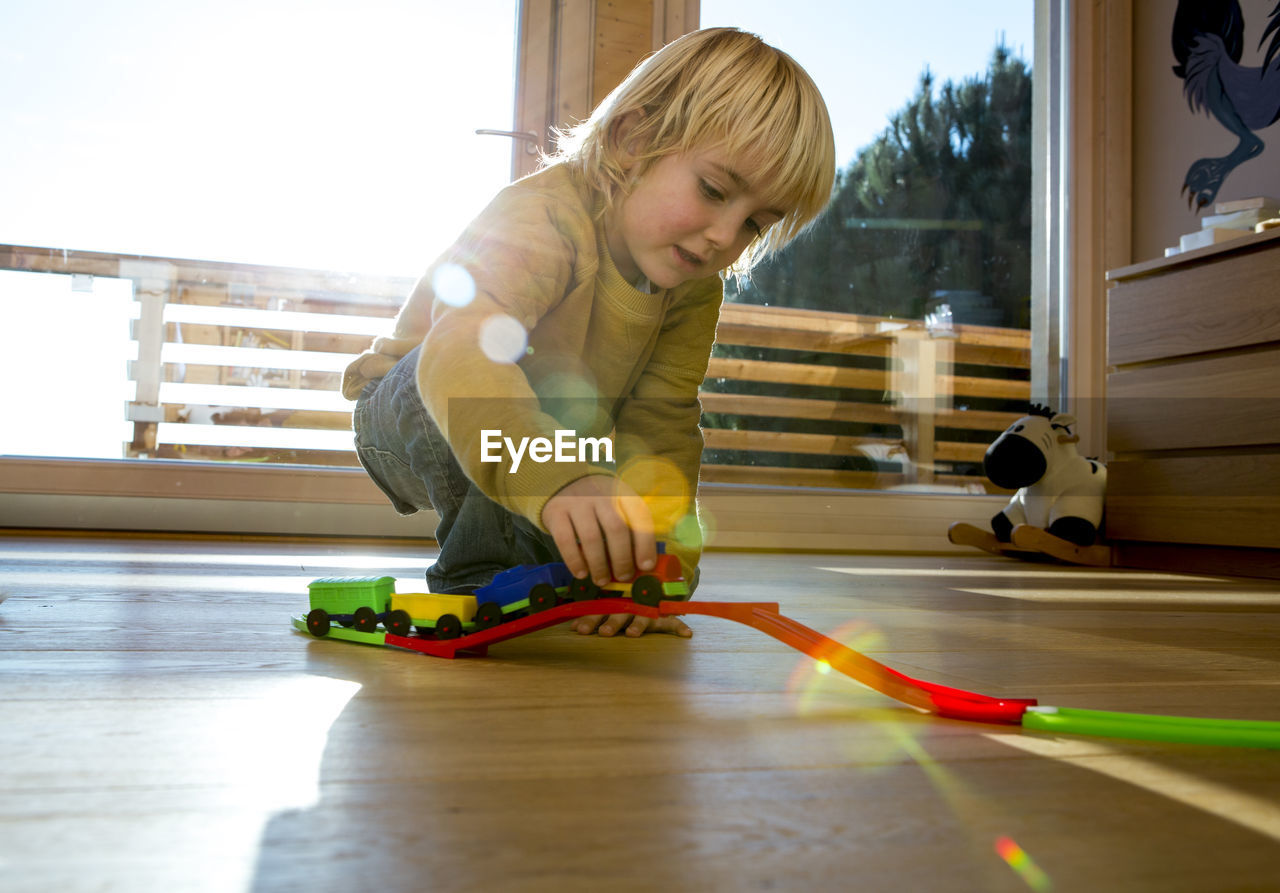 Little boy playing with toy train on the wooden floor at home