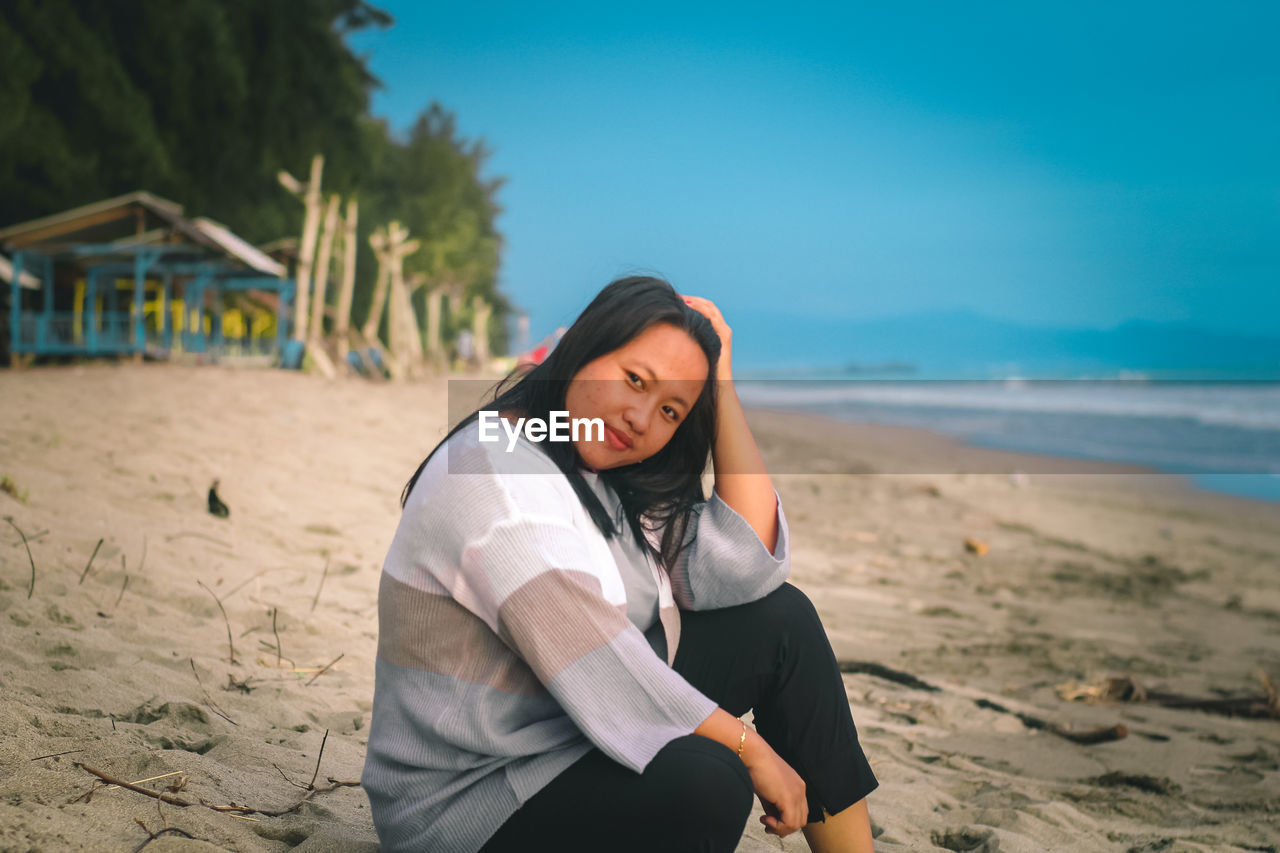 Young woman standing on beach against sky