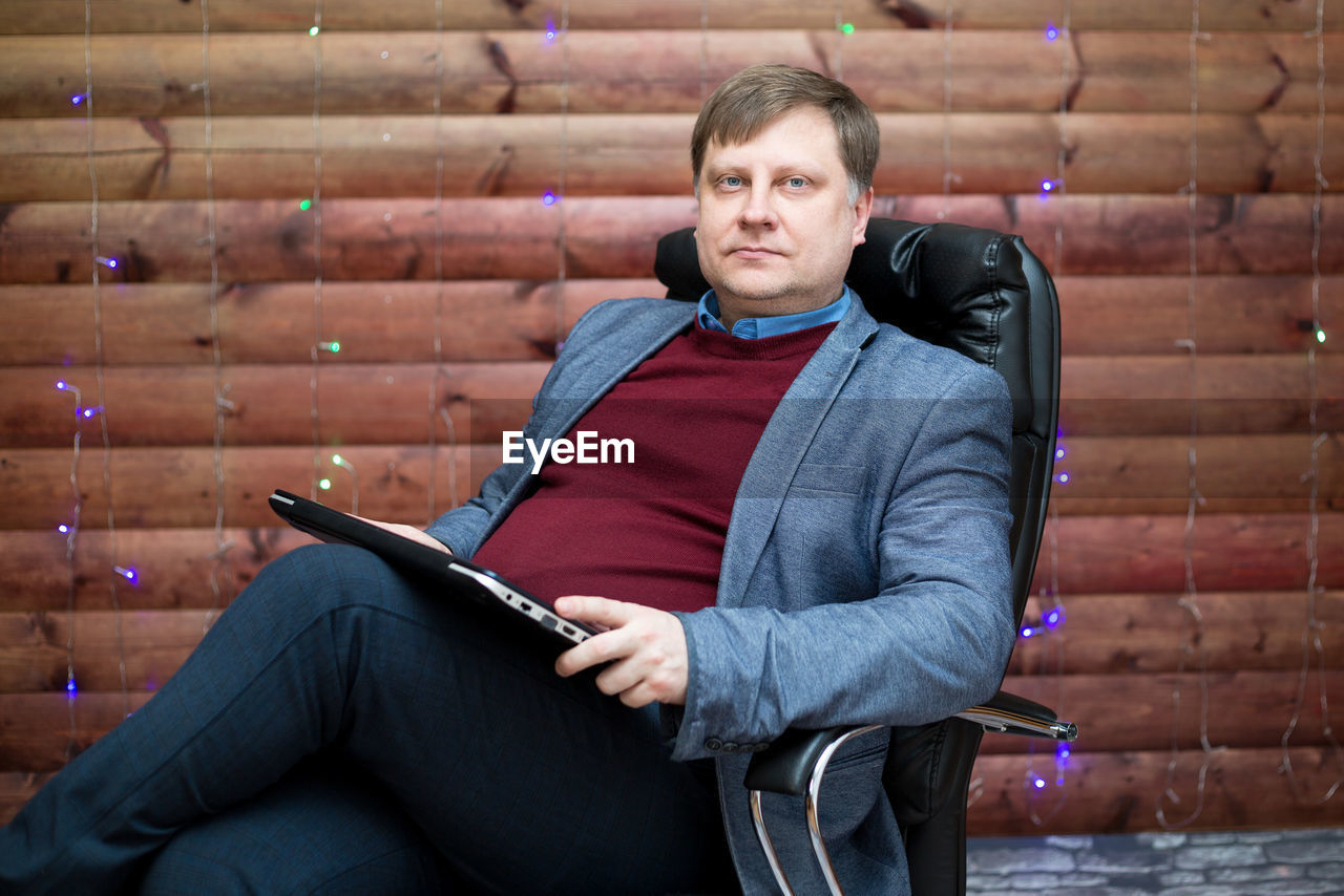 adult, sitting, one person, person, men, relaxation, blue, clothing, brick, brick wall, wireless technology, technology, lifestyles, communication, wall, casual clothing, digital tablet, portrait, business, human face, looking, three quarter length, architecture, activity, computer, leisure activity, indoors, holding, emotion, serious, copy space, photo shoot