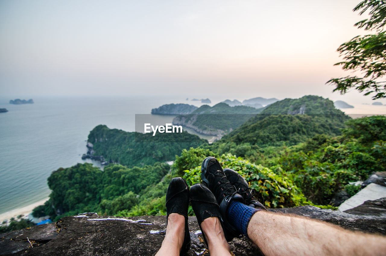 Low section of friends sitting on cliff against sea