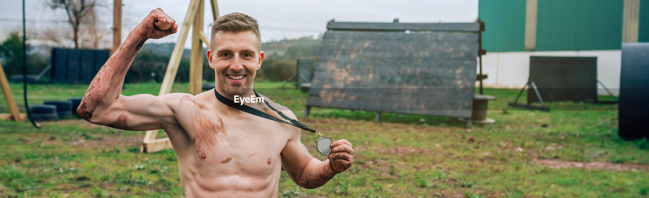 Portrait of shirtless man holding medal on land