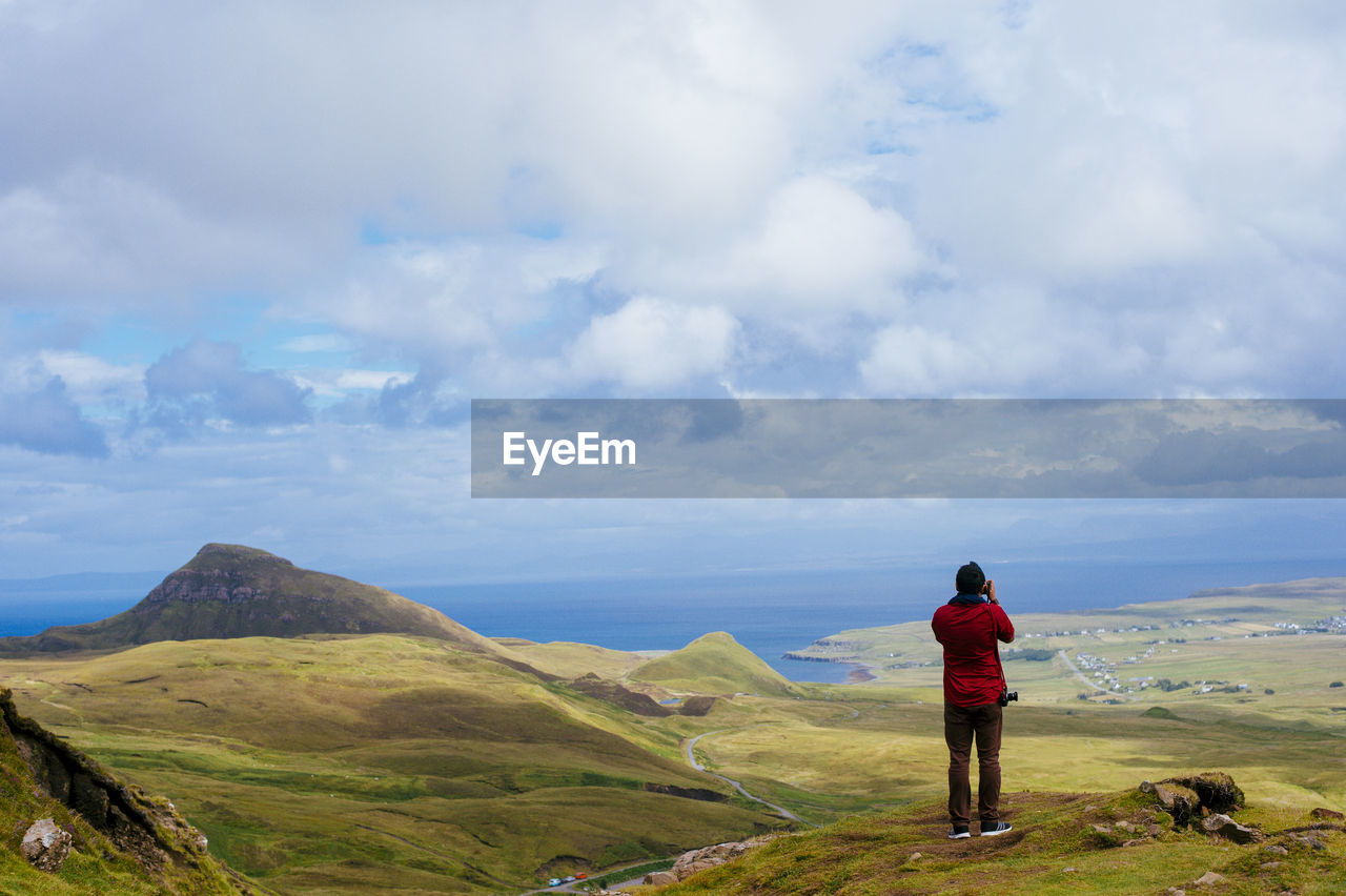 Rear view of man standing on mountain by sea against sky